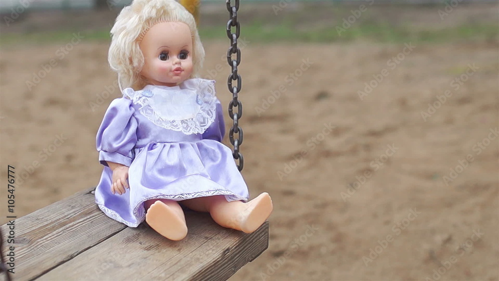 Doll in blue and purple dress swinging on a swing in the summer Doll in blue and purple dress swinging on a swing in the summer