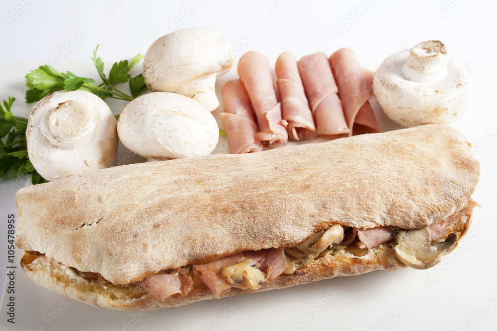Fototapeta premium Delicious sandwich with grilled ham, button mushrooms and cheese in a bun placed beside fresh button mushrooms and ham.