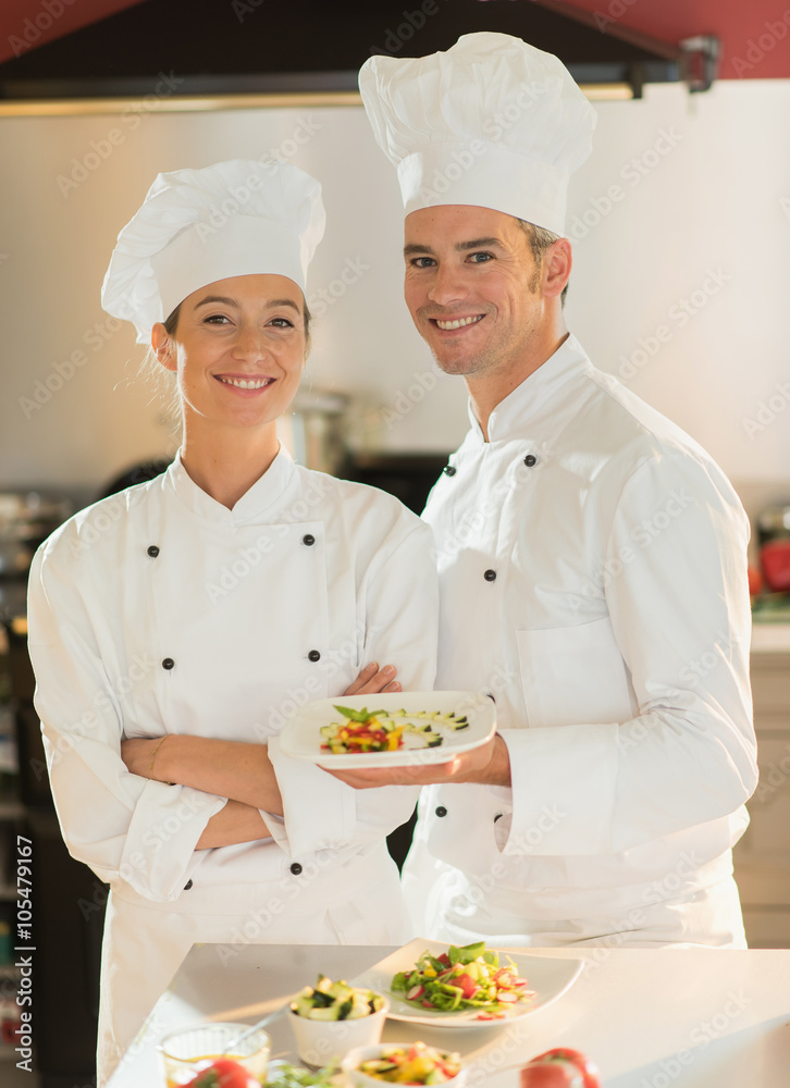 Two smiling chefs in a kitchen presenting a plate of fine food. Two smiling chefs in a kitchen presenting a plate of fine food.