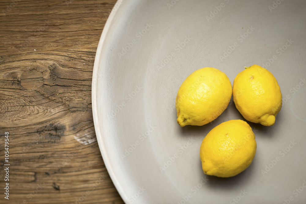 Three lemons in a shallow stoneware bowl on a wooden surface Three lemons in a shallow stoneware bowl on a wooden surface