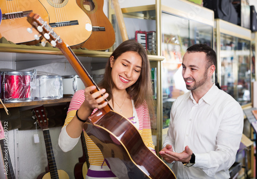Friendly positive shopgirl helping male client to select guitar