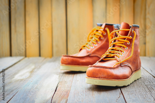 A pair of brown leather boots with laces placed on wooden floor, selective focus