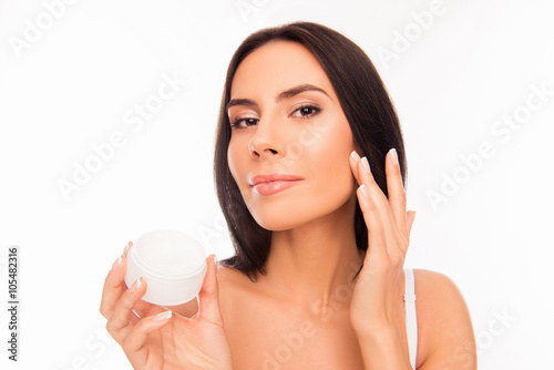 Beautiful pretty young woman applying cream on her face