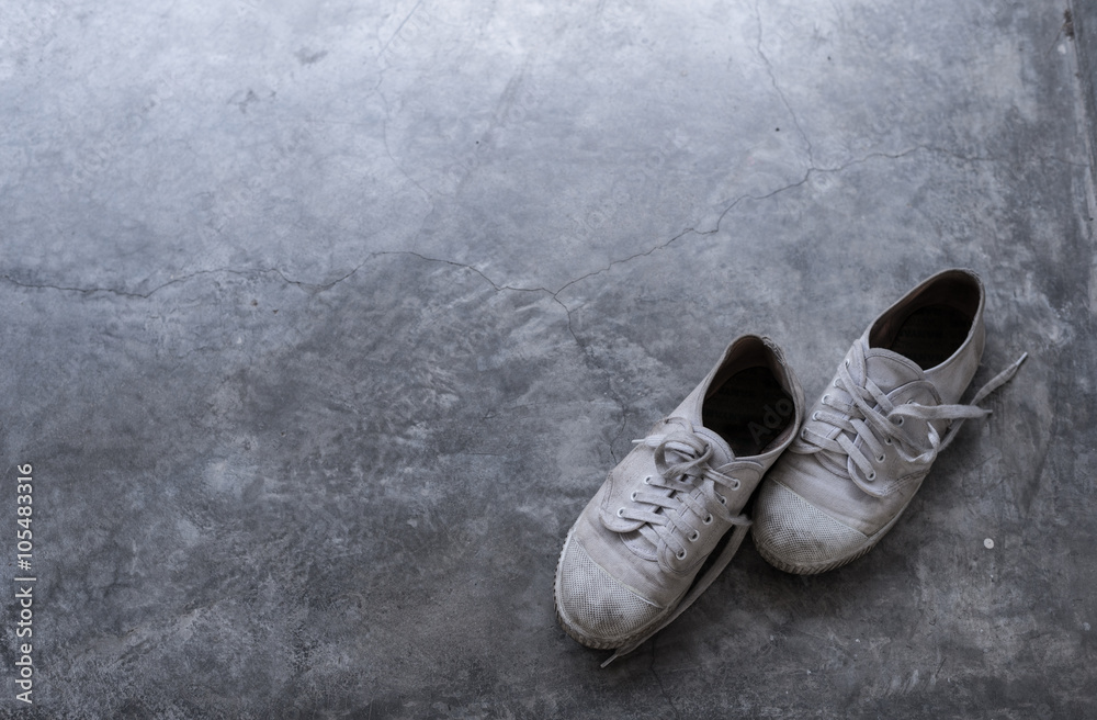 A pair of old dirty shoes on the cement floor with light shading from the corner. A pair of old dirty shoes on the cement floor with light shading from the corner.