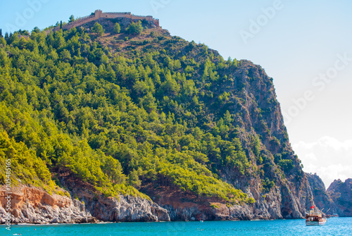 Beach of Cleopatra with sea and rocks of Alanya peninsula, Antalya, Turkey. Beautiful landscape of tourist destination with high green cliff and Castle of Alanya.