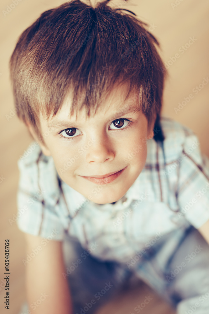 Closeup portrait of handsome smiling little boy with brown eyes wearing checkered shirt sitting on floor looking at camera. Happy childhood concept, selective focus on eyes, top view Closeup portrait of handsome smiling little boy with brown eyes wearing checkered shirt sitting on floor looking at camera. Happy childhood concept, selective focus on eyes, top view