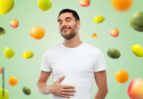 happy full man touching tummy over falling fruits