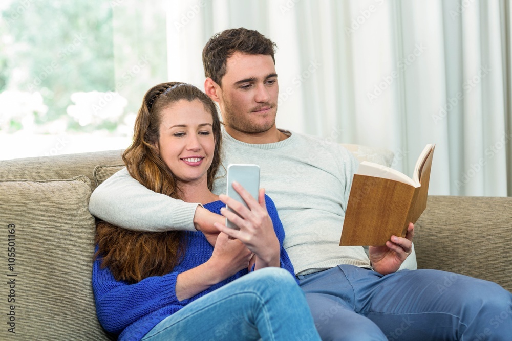 Young couple sitting on sofa and using mobile phone