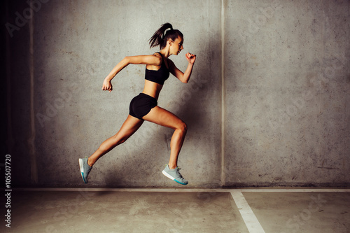 Slim attractive sportswoman running against a concrete wall
