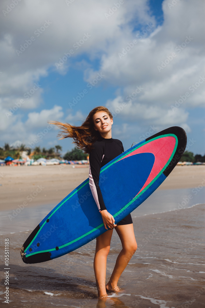 young girl in a black wetsuit with surfboard awaits brought waves for surfing, surfing at sunset, catch the wave, ride the wave sports fitness, sandy beach ocean bali indonesia
