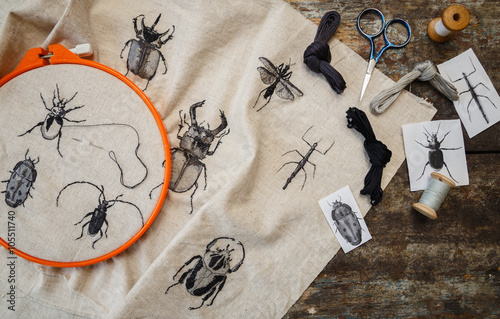 Embroidery in process with hoop and sewing threads on table. Embroidered beetles.