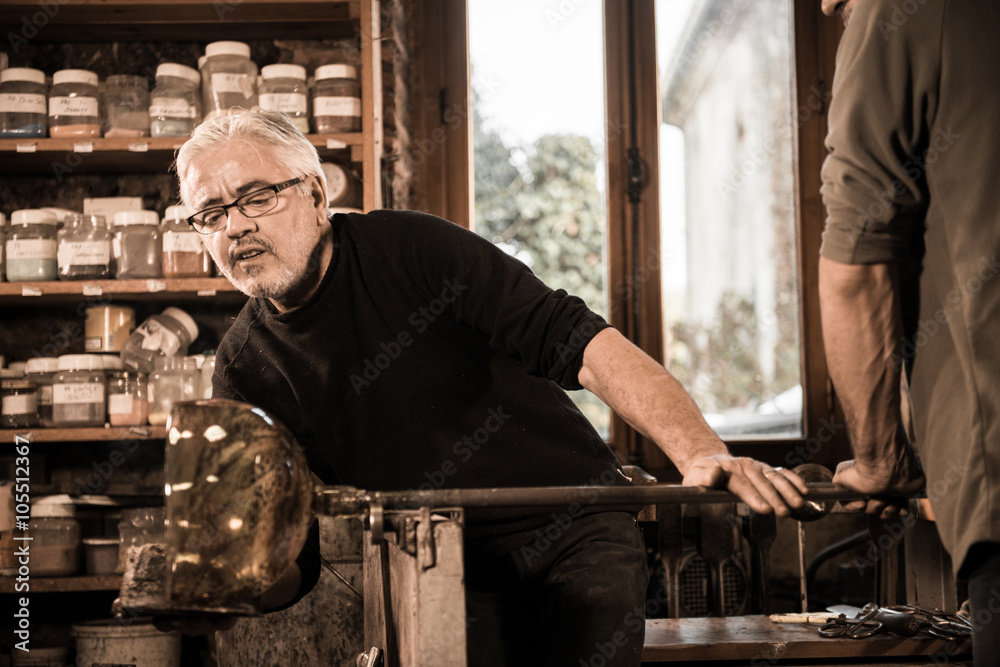 Glassblower forming molten glass in his worshop Glassblower forming molten glass in his worshop