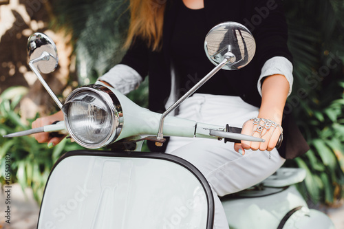 young girl with long hair in sunglasses in a black t-shirt tattoo on his shoulder in white pants with red lipstick posing on a retro scooter Vespa colors taifani vintage style straw hat with a stylish © armada1985