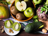 Fresh green fruit and vegetables on wooden table - apples, kiwi, pears, mango, avocado and artichokes