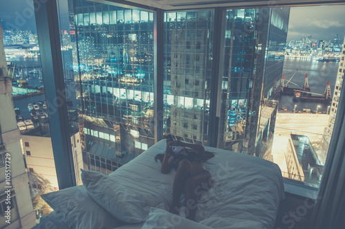 Young beautiful woman lying in the bed,making selfie or reading messages or chatting at night.Luxurious apartment with french windows,breathtaking view over harbour,skyscraper.Addiction to internet photo
