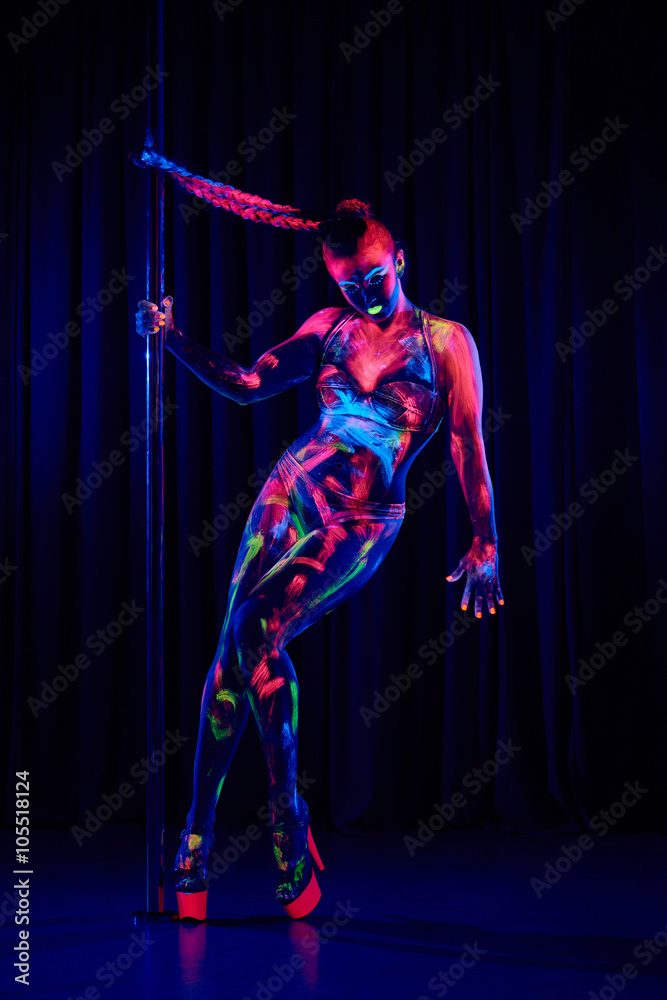 Female pole dancer in bright neon colours under ultraviolet (UV) light on background