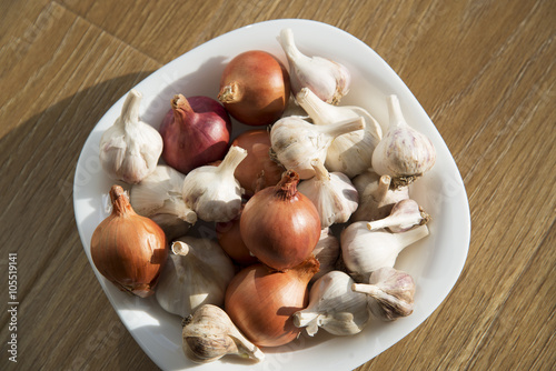Garlic and onions in a white plate on a wooden background.