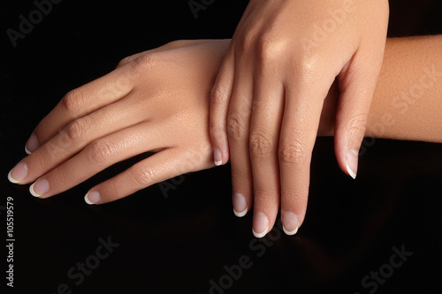 Beautiful female arms with ideal french manicure on black background. Care about female hands, healthy soft skin. Spa & cosmetics. Beauty care. Close-up of beautiful famele fingers with nails polish