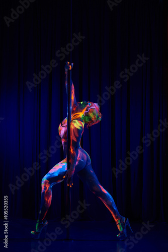 Female pole dancer in bright neon colours under ultraviolet (UV) light on background