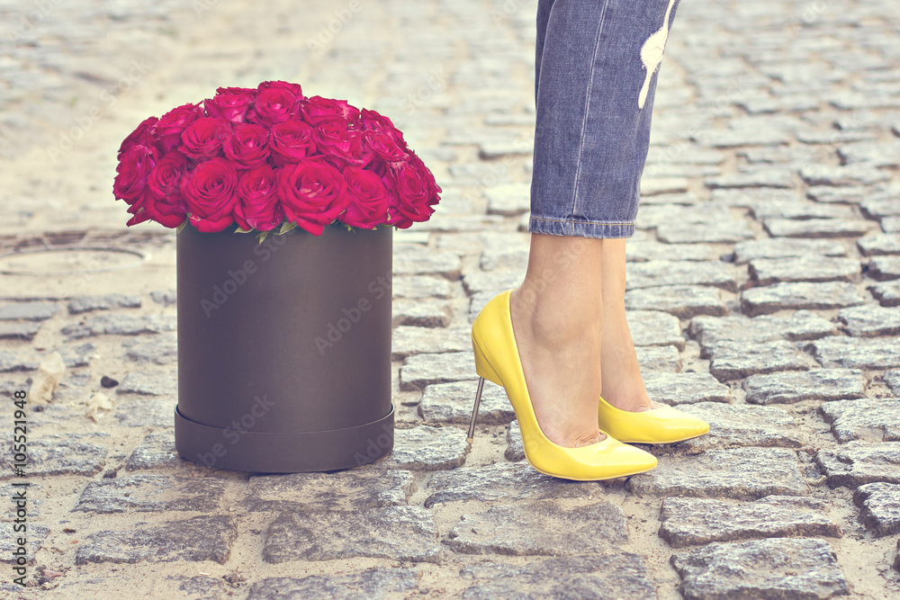 The bouquet of red roses and female legs in jeans and yellow shoes with heels.