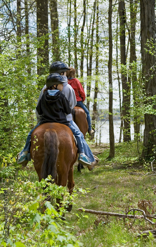 Family of Horseback Riders – A family of one adult and two children ride their horses in the forest, on the trail.