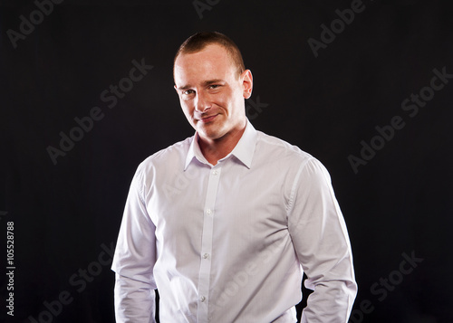 Young smiling man in white shirt over dark background