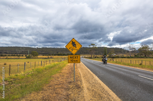 Motorcyclist on the road with Warning Sign on the A3 road between Swansea and Triabunna, Tasmania, Australia. photo