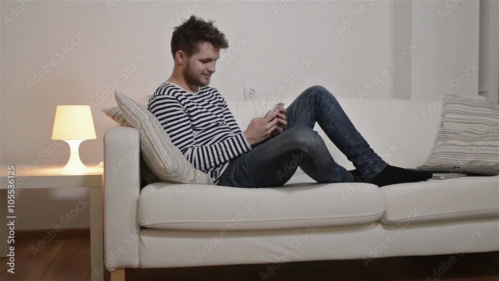Young man with smartphone texting, sitting on the couch Young man with smartphone texting, sitting on the couch