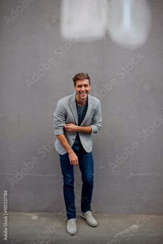 Handsome man in grey jacket standing near the wall and smiling