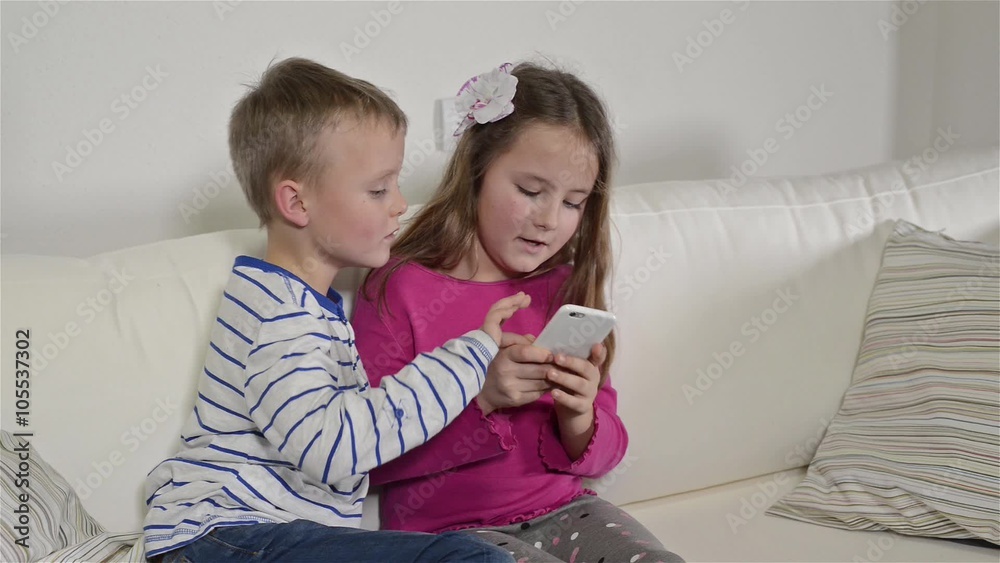 Children at home sitting on sofa, playing with smartphone Children at home sitting on sofa, playing with smartphone