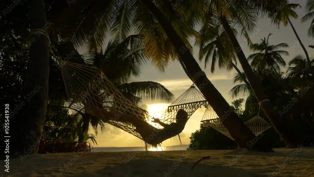 Female swinging in hammock on exotic beach at sunset