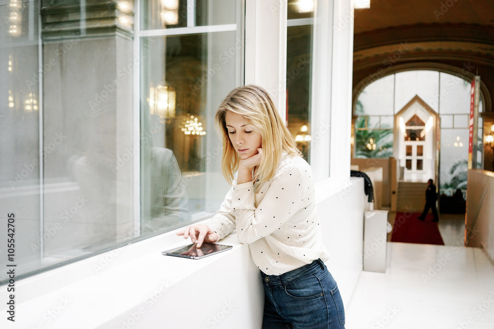 portrait of attractive young blonde businesswoman browsing internet on her touch pad inside the modern office portrait of attractive young blonde businesswoman browsing internet on her touch pad inside the modern office