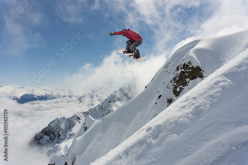 Snowboarder making jump, extreme mountain freeride.