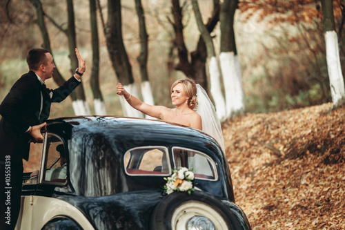 Stylish wedding couple, bride, groom kissing and hugging near retro car in autumn © olegparylyak