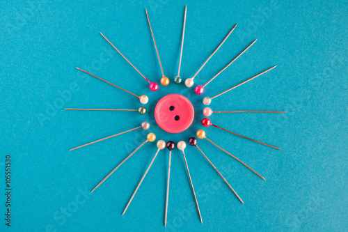 Button. Pink button surrounded by sewing pins