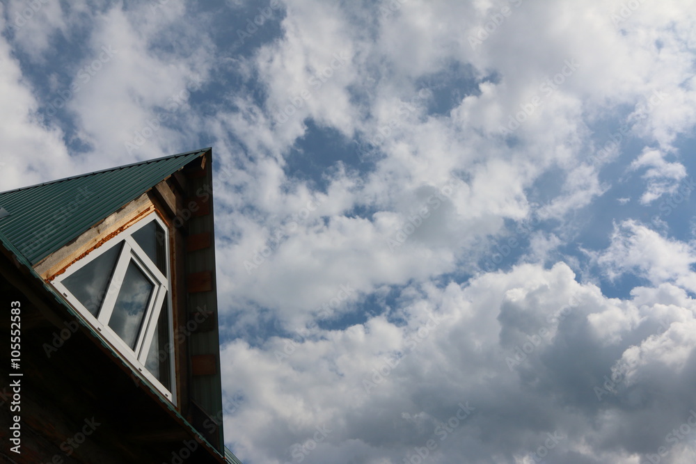 Triangular skylight of an attic of a village log house under construction against a cloudy sky