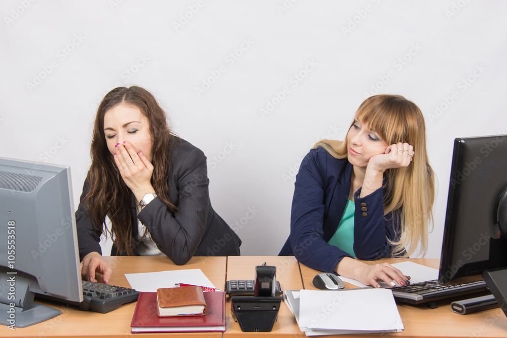 Two young office employee wearily sitting behind a desk Two young office employee wearily sitting behind a desk