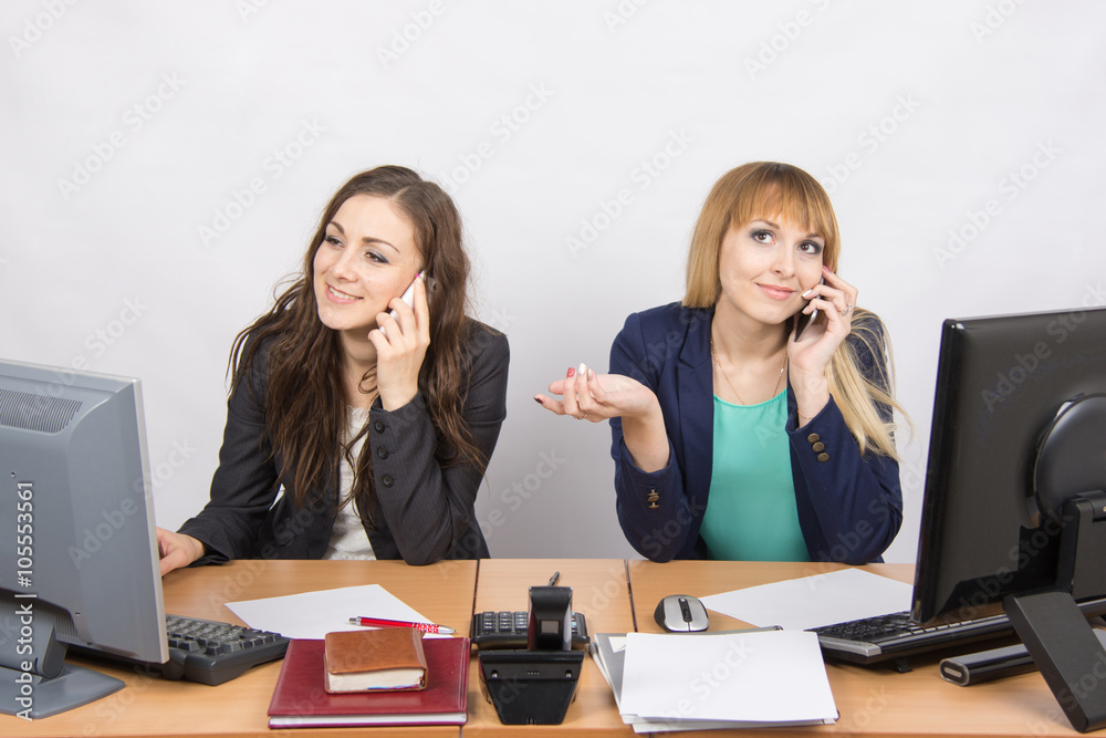 Two girls at a desk talking on mobile phone in the office Two girls at a desk talking on mobile phone in the office