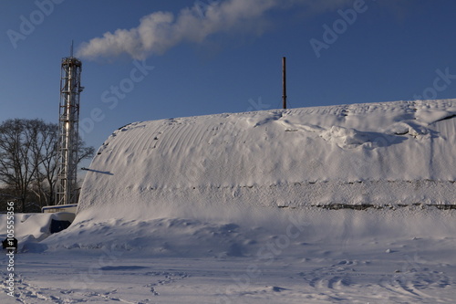 Труба с дымом и ангар, покрытый снегом, зимним солнечным днем