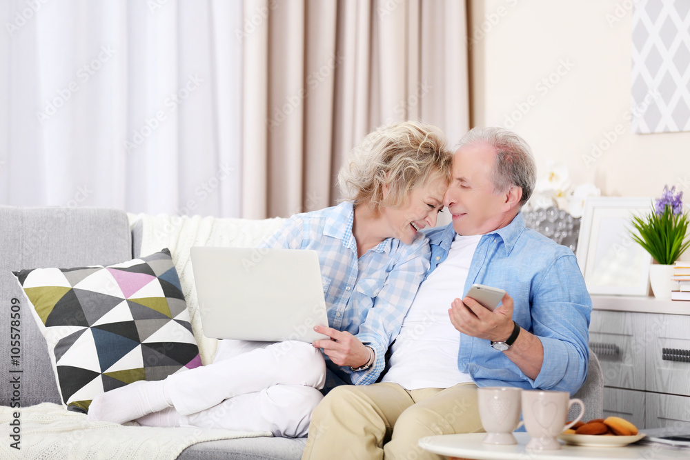 Mature couple sitting together with laptop and mobile phone at home Mature couple sitting together with laptop and mobile phone at home