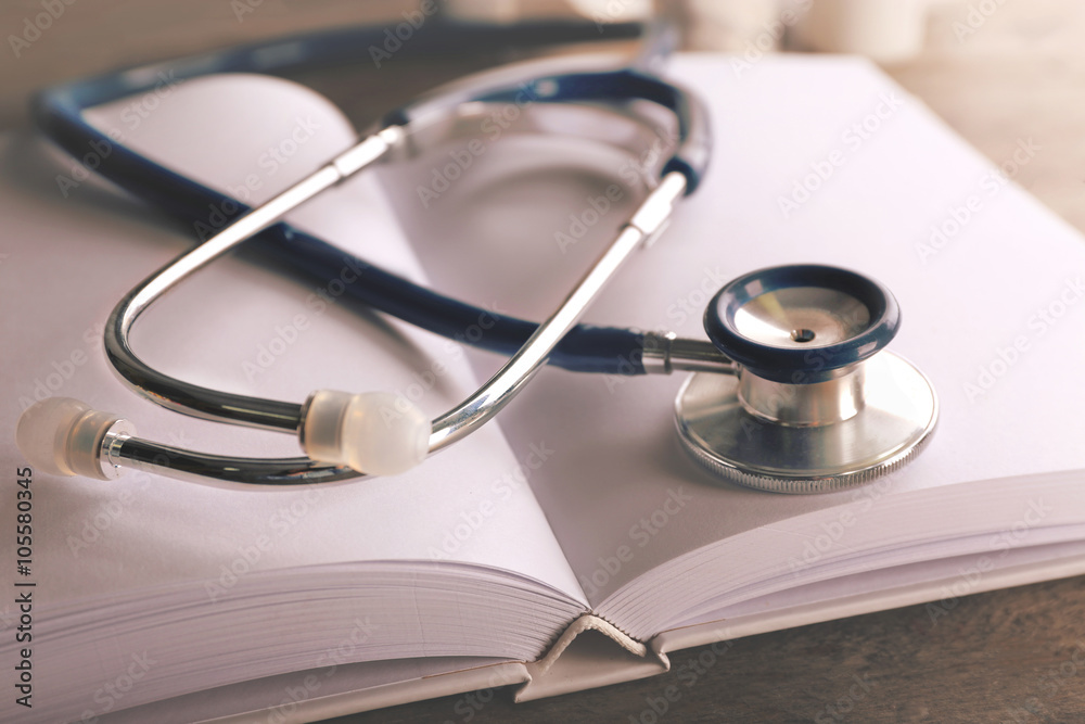 Stethoscope with open book on wooden background. Medical literature concept Stethoscope with open book on wooden background. Medical literature concept