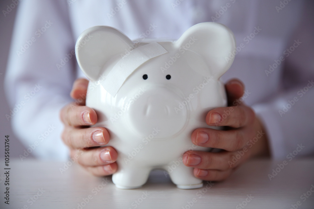 Woman holding in hands white piggy bank with patch at the table Woman holding in hands white piggy bank with patch at the table