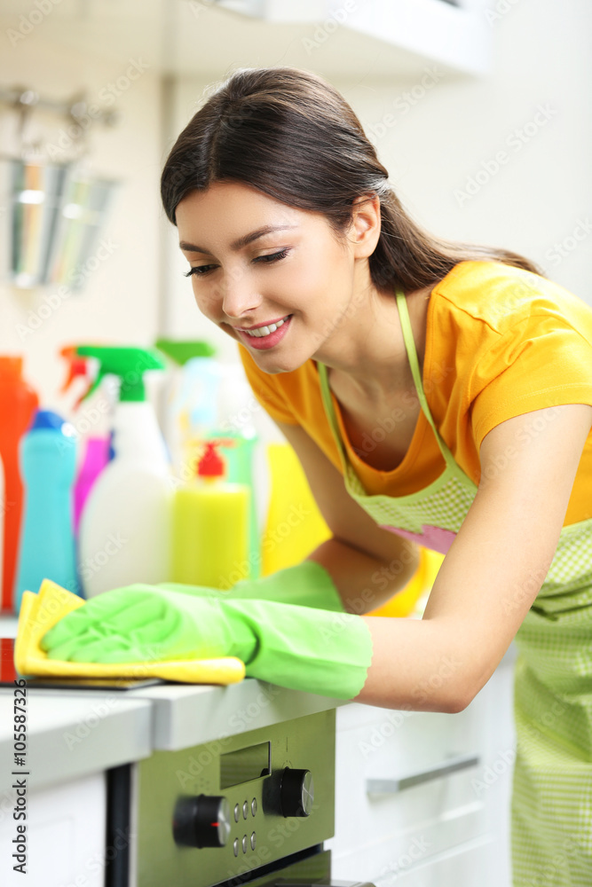 Beautiful woman in protective gloves cleaning electric range with rag