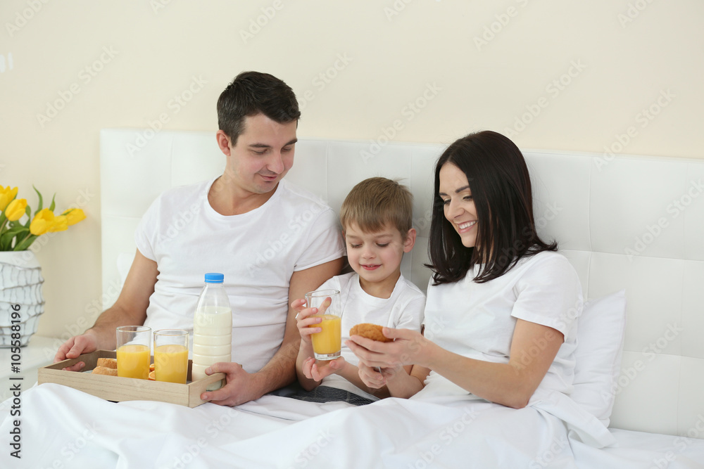 Family having breakfast with orange juice and buns in bed