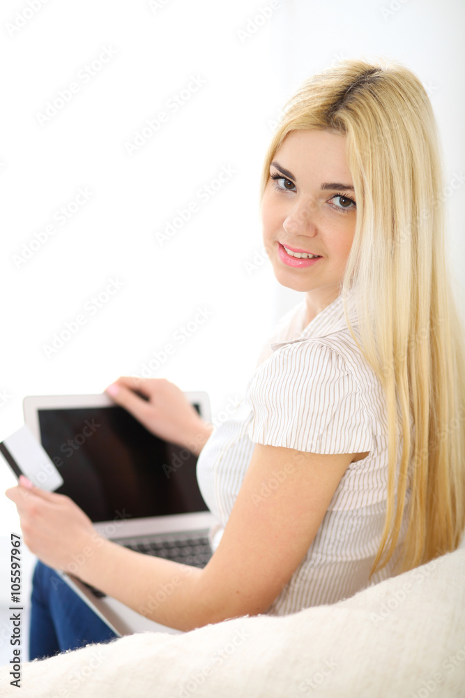Naklejka premium Happy woman doing online shopping at home . Close- up of a hand holding a credit card next to a laptop