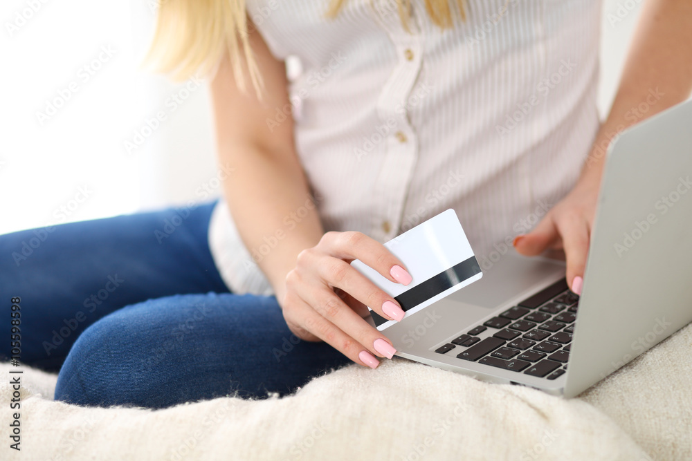 Naklejka premium Happy woman doing online shopping at home . Close- up of a hand holding a credit card next to a laptop