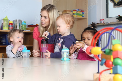 Erzieherin am Tisch Kinder trinken aus Trinkflasche mit Spielzeug photo
