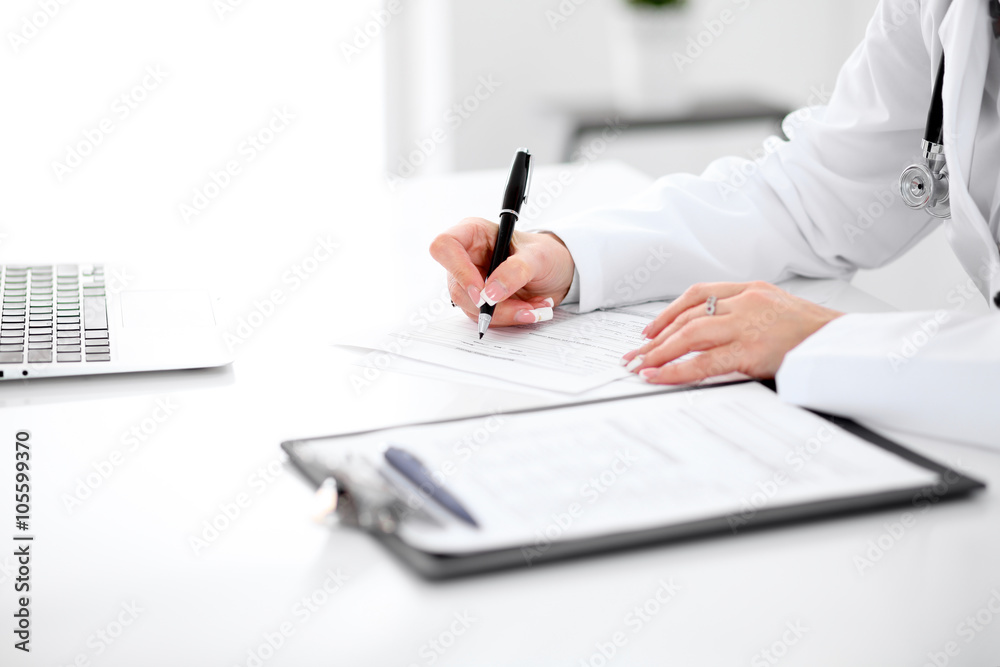Close-up of a female doctor filling out application form , sitting at the table in the hospital Close-up of a female doctor filling out application form , sitting at the table in the hospital