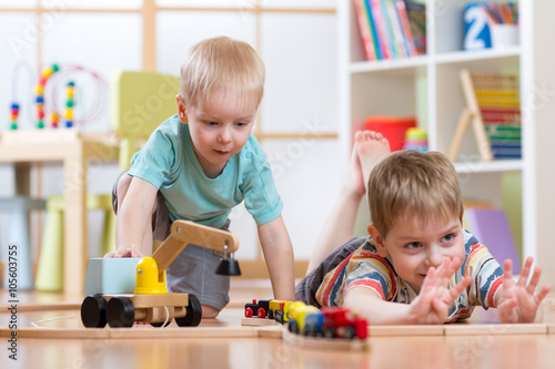 Children play with wooden train and build toy railroad at home, kindergarten or daycare