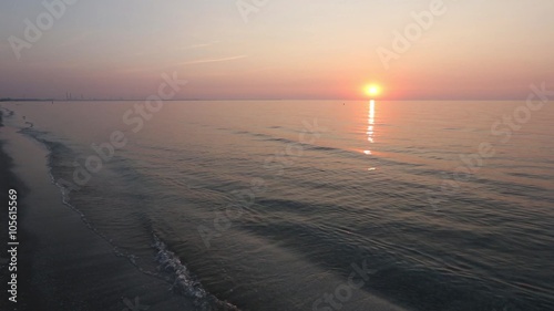 The sun rising over horizon and calm sea water surface with suntrack. View from sandy beach. There is surf noise.
 photo